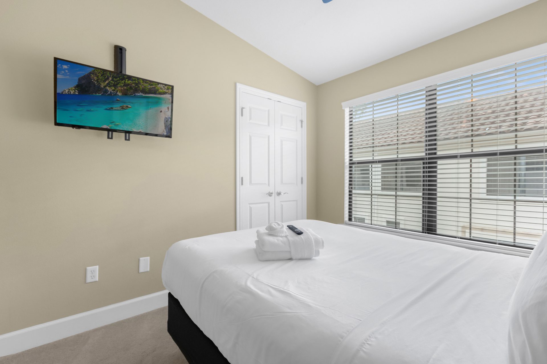 Bright guest bedroom with mounted TV and vaulted ceiling